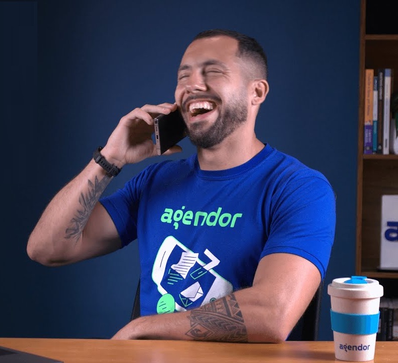 Vendedor B2B do Agendor no telefone com um cliente, em ambiente de escritório.