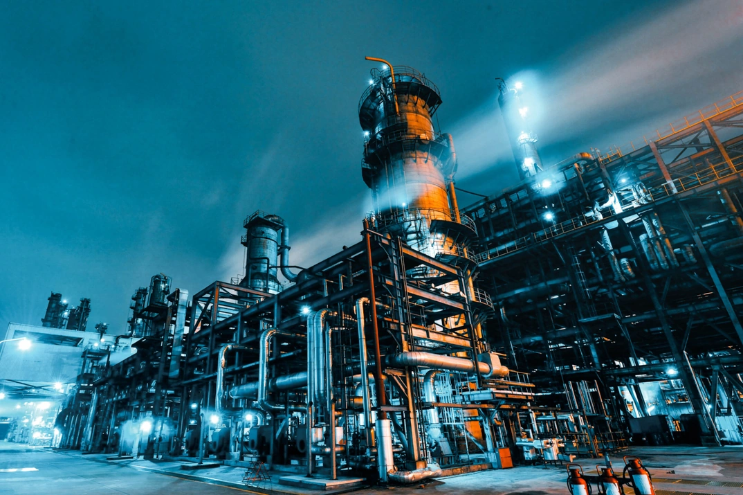 Refinaria industrial à noite com iluminação azul e estruturas metálicas