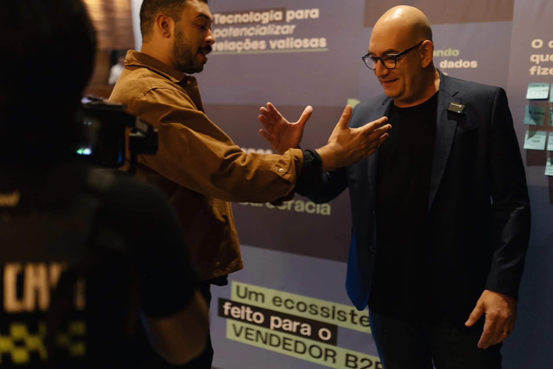 Dois consultores parceiros conversando durante um evento do Agendor, diante do painel da marca.
