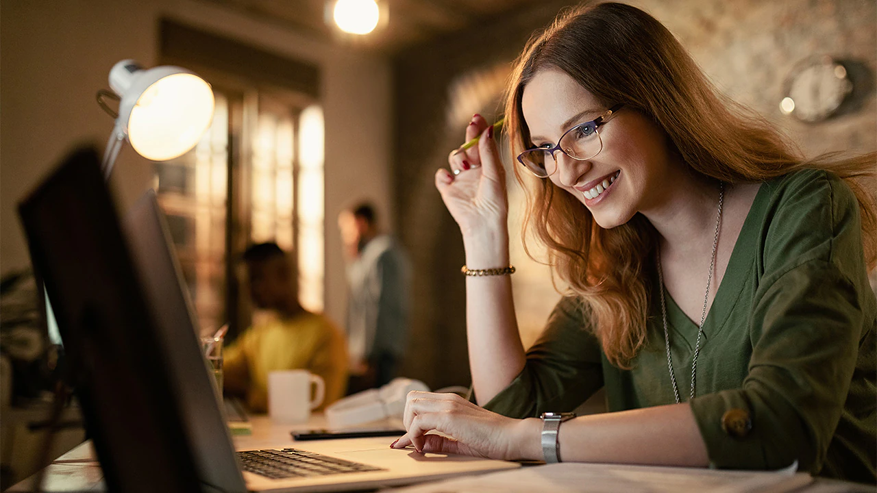 Analista comercial sorrindo diante do computador enquanto lê o relatório mensal de inteligência setorial.